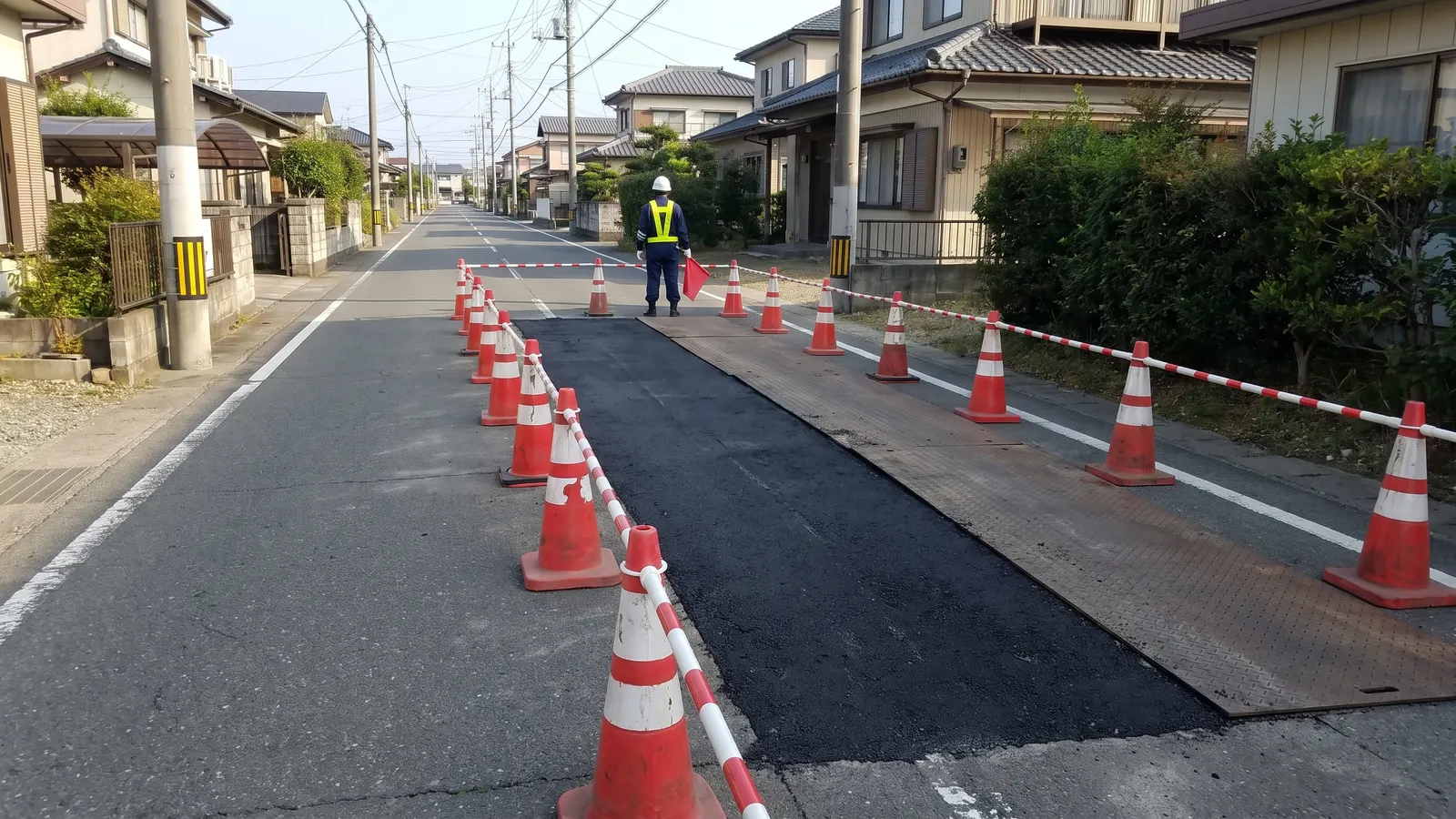片側を止めた道路の工事で、赤い旗を持って立つ警備員の後ろ姿