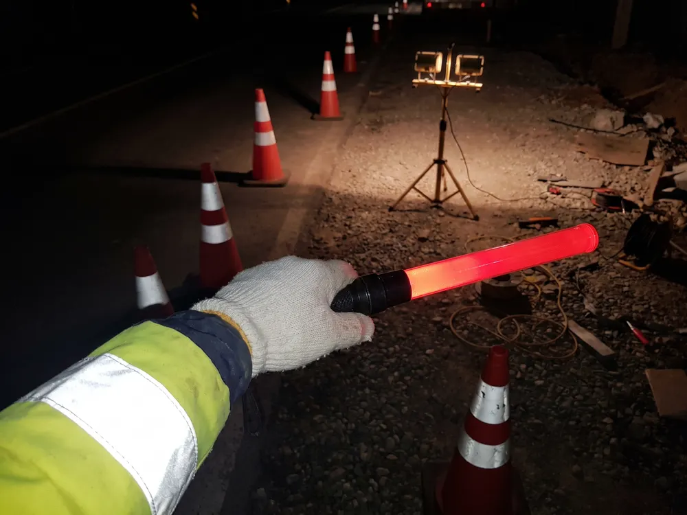 夜の工事の現場で、光る誘導灯を持つ手