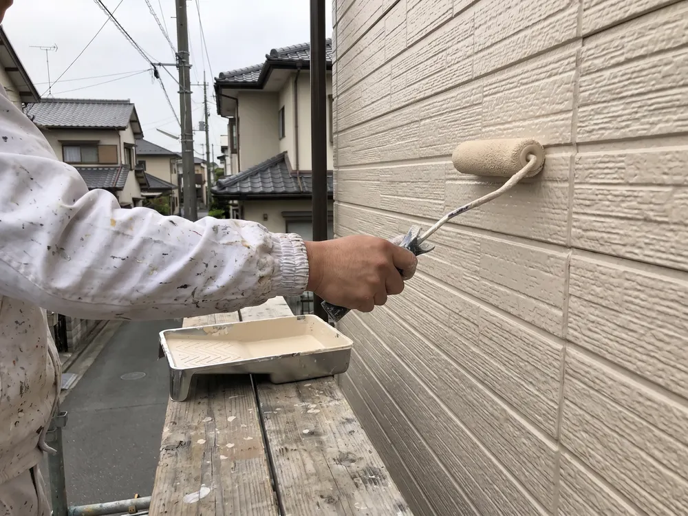 外壁にローラーで塗料を塗る職人の手