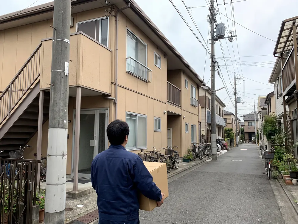 集合住宅の入口へ箱を運ぶ配達の人の後ろ姿