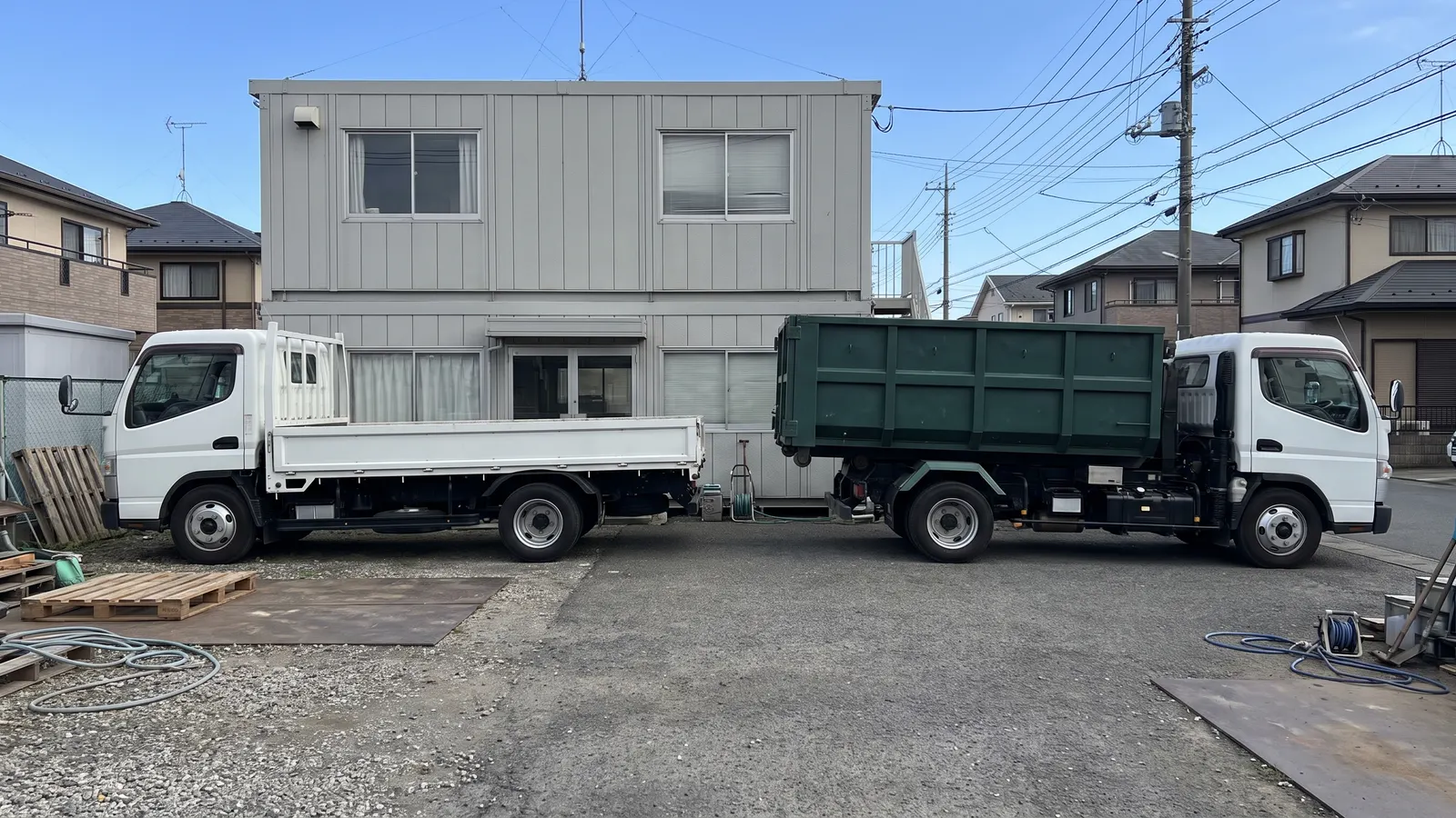 車庫に並んだ白いトラックと、緑のコンテナを積んだ車