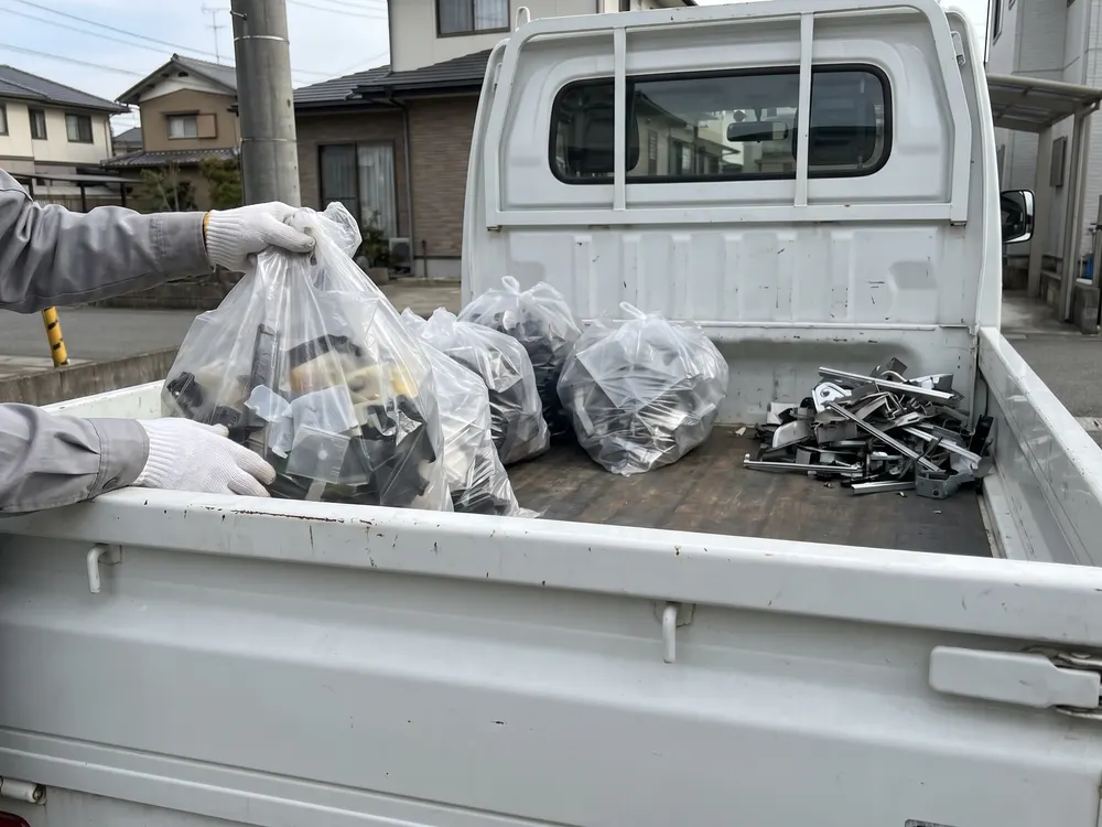 軽トラックの荷台に、袋と金属くずを分けて積む手元