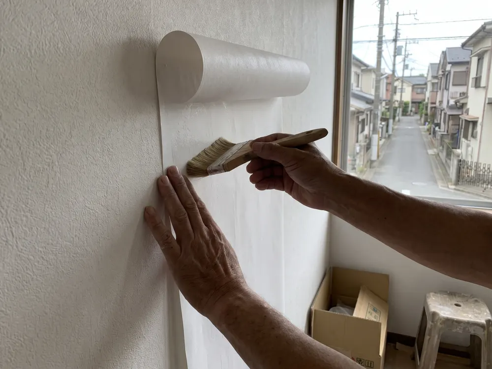 白い壁紙をはけでなでつける職人の手